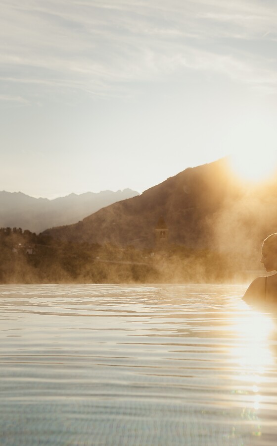 Frau im Pool bei Sonnenaufgang mit Bergblick