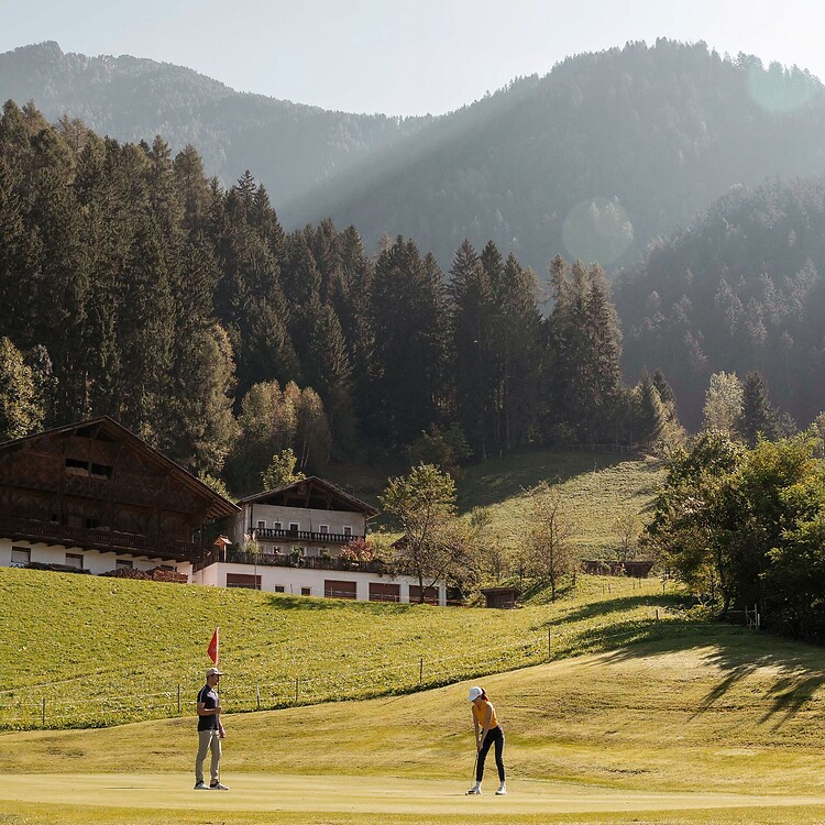 Uomo e donna giocano a golf davanti alle Alpi