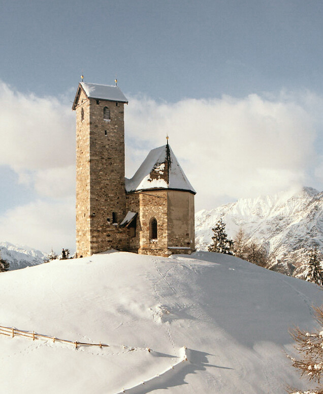 Chiesetta su collina in inverno con neve e panorama montano
