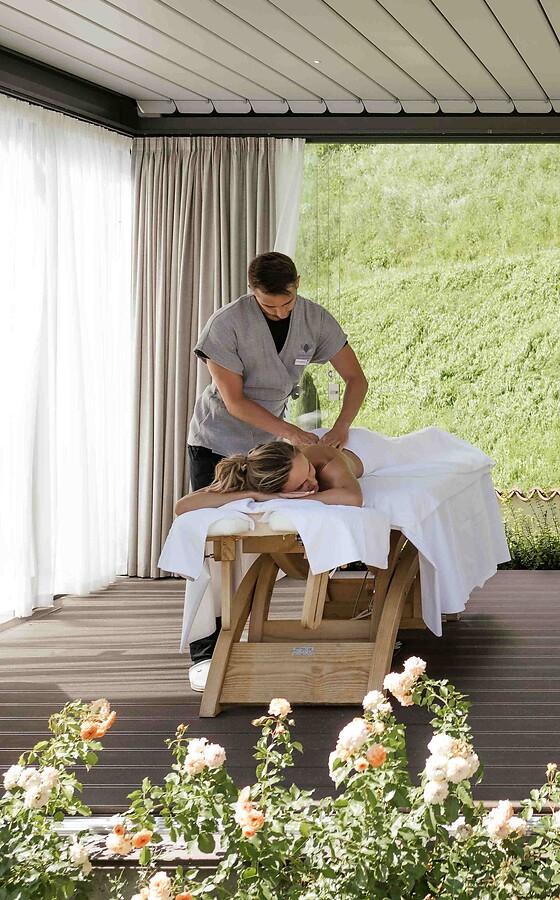 Woman and man being massaged in the garden pavilion among blooming flowers