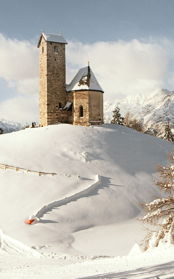 Small church on hill in winter with snow and mountain panorama