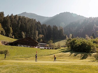 Man and woman playing golf in front of the Alps