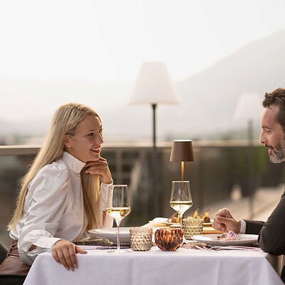 Woman and man having romantic candlelight dinner on rooftop terrace with mountain panorama