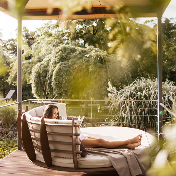 Frau liegt entspannt auf der Hängeliege im großzügigen Hotelgarten