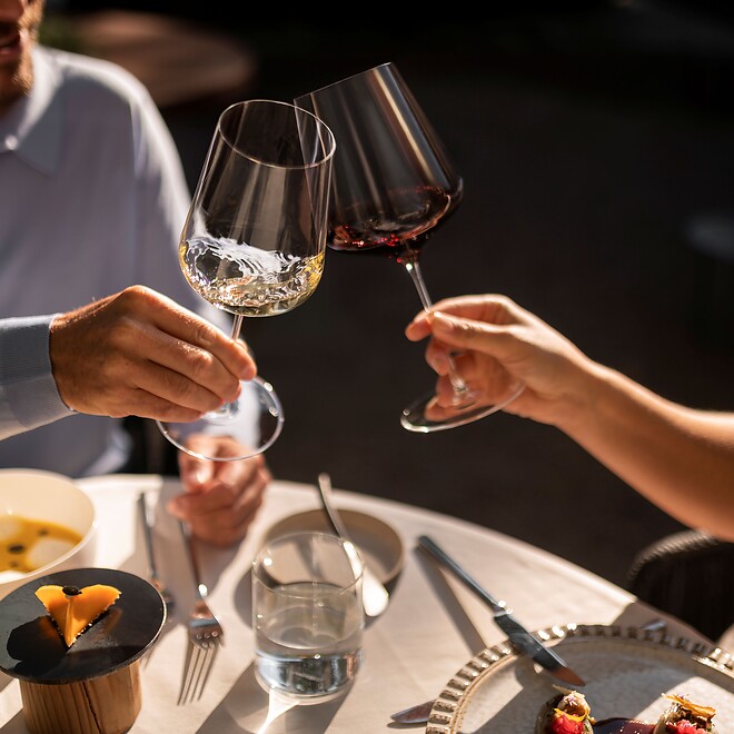 Mann und Frau stoßen bei einem Glas Wein an und genießen gutes Essen