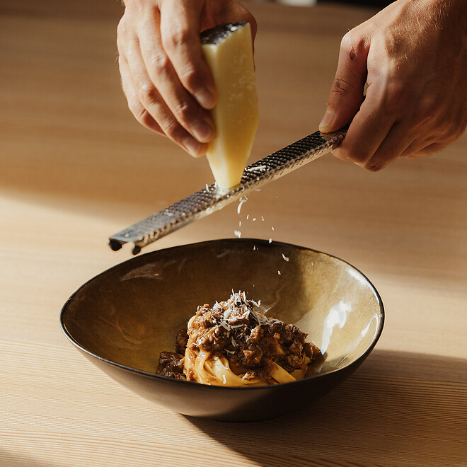 Servicekraft reibt Parmesanläse über die frische Pasta