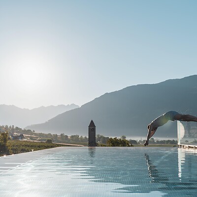 Mann springt in Sky Infinity Pool vor Bergkulisse und tiefstehendem Sonnenlicht