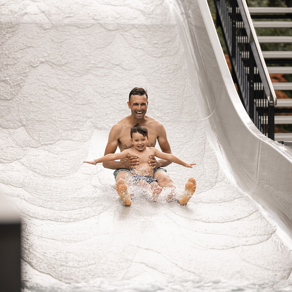 Il padre e il figlio scendono dallo scivolo acquatico a onde nel giardino dell’hotel.