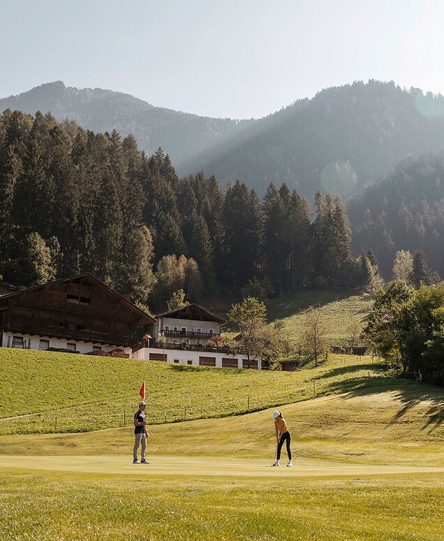 Man and woman playing golf in front of the Alps