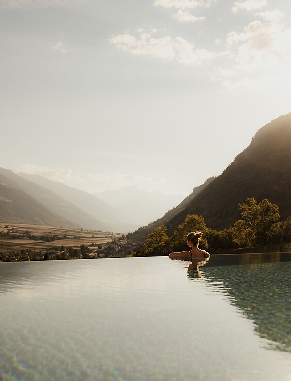 Frau genießt im Infinity Pool bei Sonnenuntergang die Panoramaaussicht