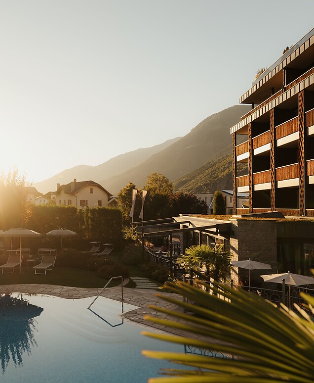 Hotelfassade mit Pool und Palmen beim Sonnenuntergang