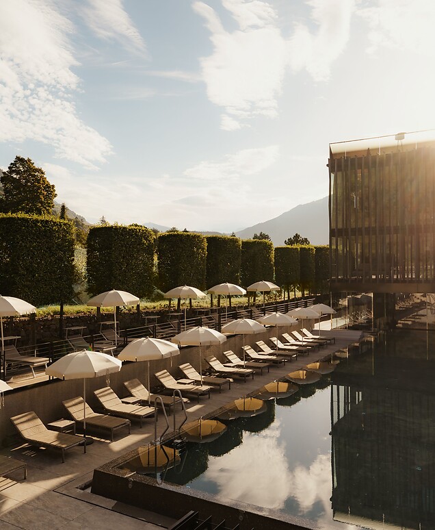 Sportpool mit Sonnenliegen und Bergblick, im Hintergrund der Wellnesstower bei Sonnenaufgang