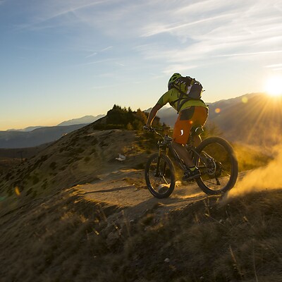 Mountainbiker fährt über erdigem Trail im Berg bei Sonnenuntergang