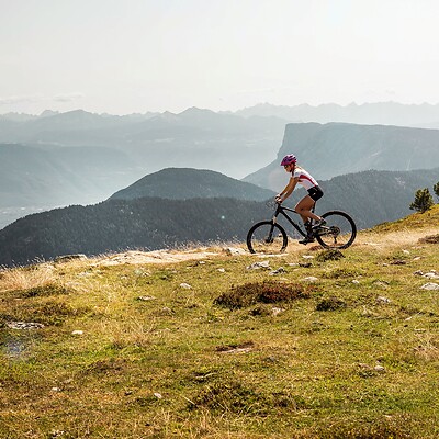 Frau fährt mit E-Mountainbike über Bergtrail vor Bergpanorama