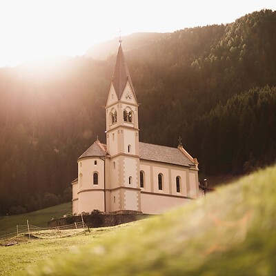 Kirche auf Waldlichtung im Berg bei tiefstehender Sonne