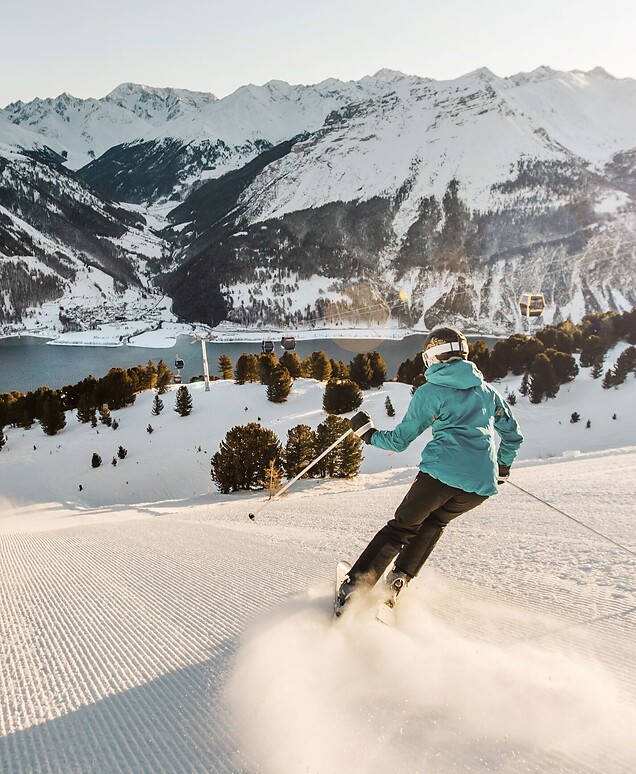 Skifahrer auf Abfahrt vor Bergkulisse bei tiefstehender Sonne