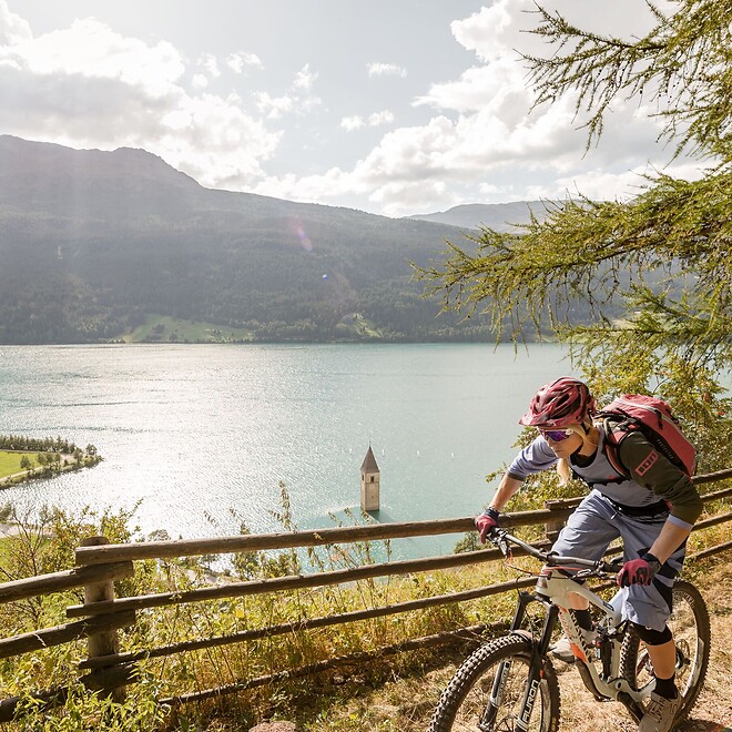 Mann und Frau biken auf Trail über dem Reschensee