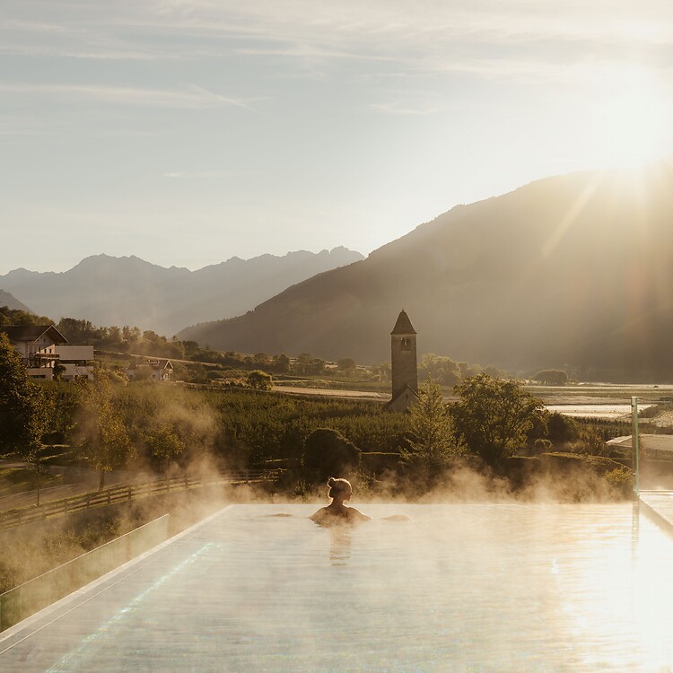 Frau genießt im Infinity Skypool die traumhafte Aussicht bei Sonnenaufgang