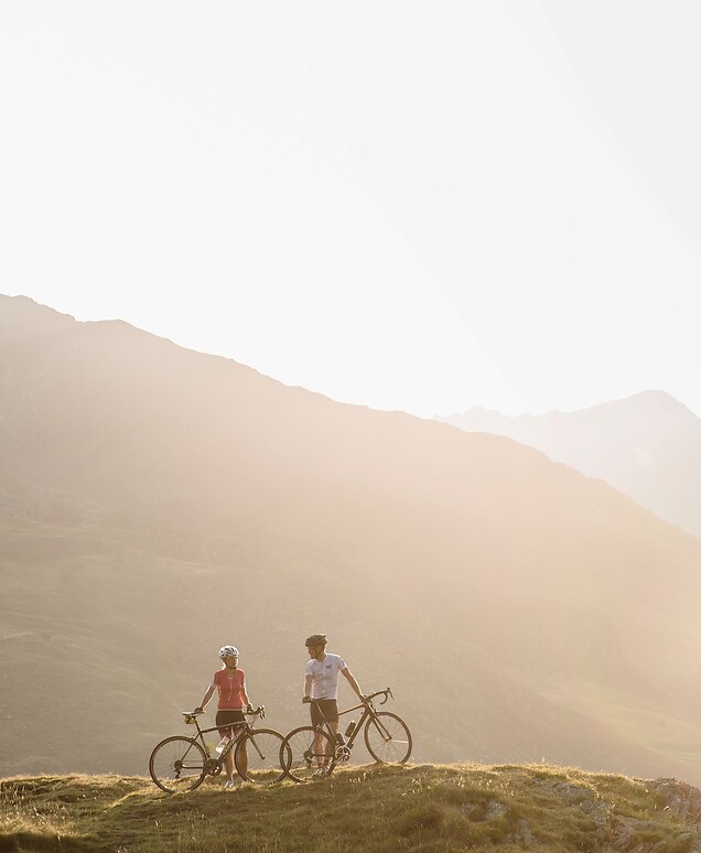 Frau und Mann mit Rad im Berg vor untergehender Abendsonne