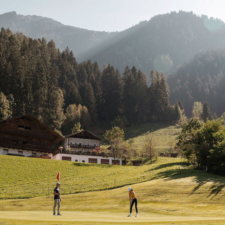 Mann und Frau beim Golfspiel vor den Alpen