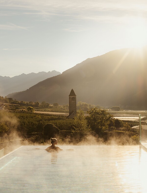 Frau genießt im Infinity Skypool die traumhafte Aussicht bei Sonnenaufgang