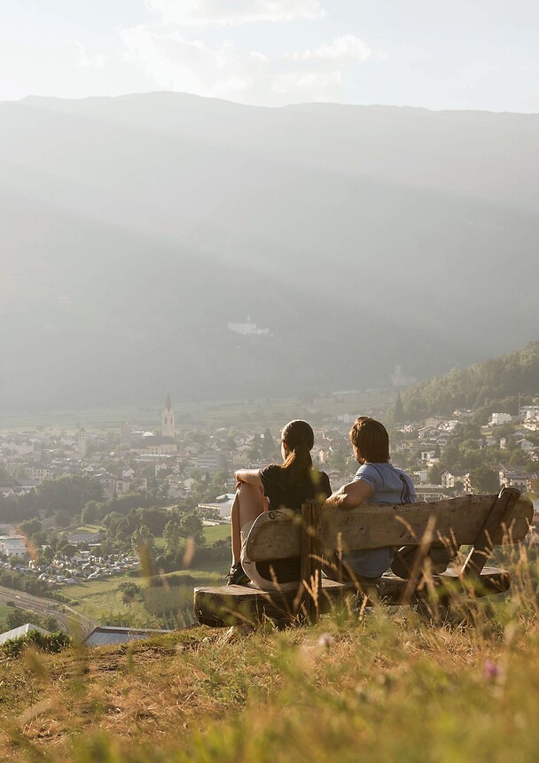 Woman and man sitting on bench in mountains overlooking valley and mountains