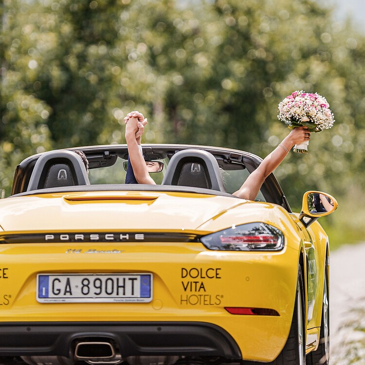 Woman and man driving yellow Porsche convertible on honeymoon