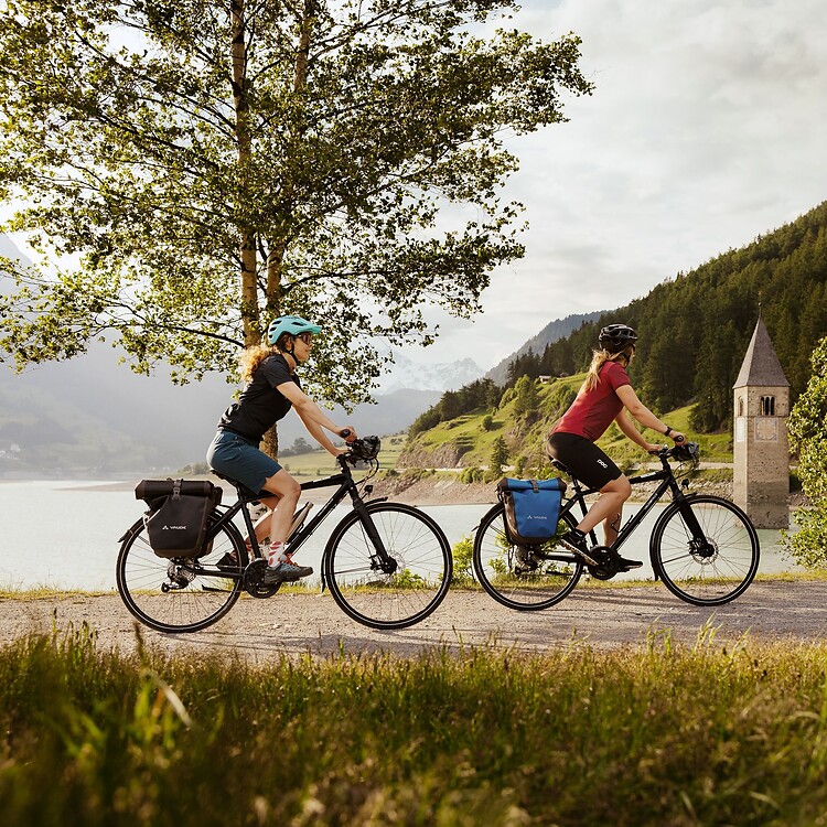 Zwei Frauen radeln mit E-Bike vorbei am versunkenen Turm im Reschensee