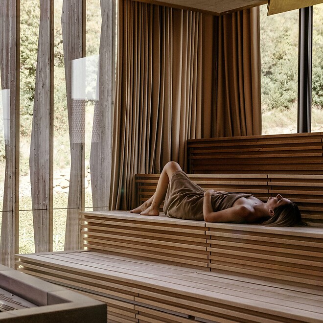 Frau liegt in der Sauna mit Aussicht auf Thermalgarten