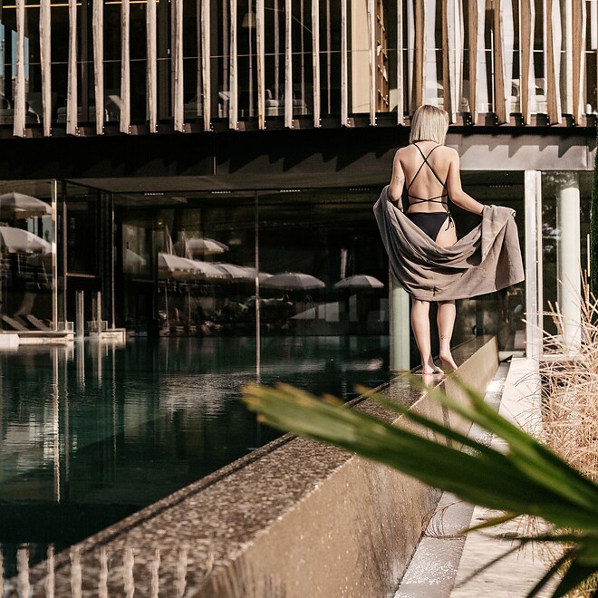 Ein moderner Außen-Sportpool im Hotel Lindenhof, überragt von dem markanten Wellnesstower mit seiner markanten vertikalen Holzlamellen-Fassade, eingebettet in eine mediterrane Gartenanlage.