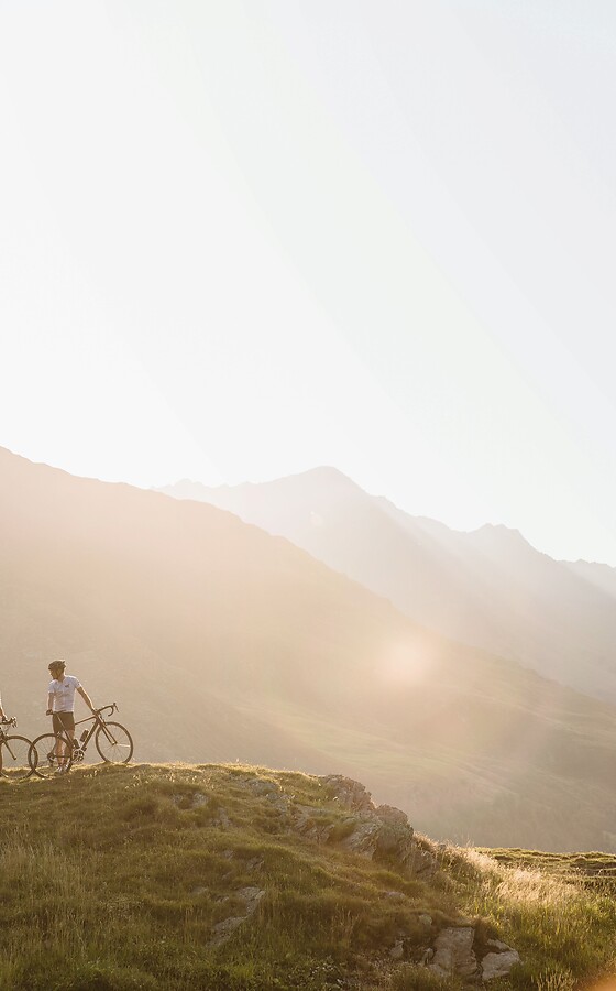 Frau und Mann mit Rad im Berg vor untergehender Abendsonne