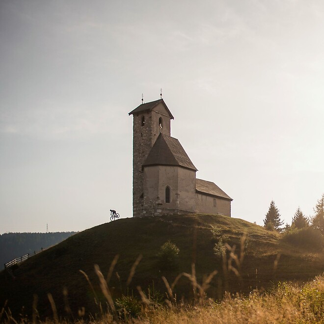 Radfahrer fährt bei Sonnenuntergang den Berg nahe der Kirche am Vigiljoch hinab